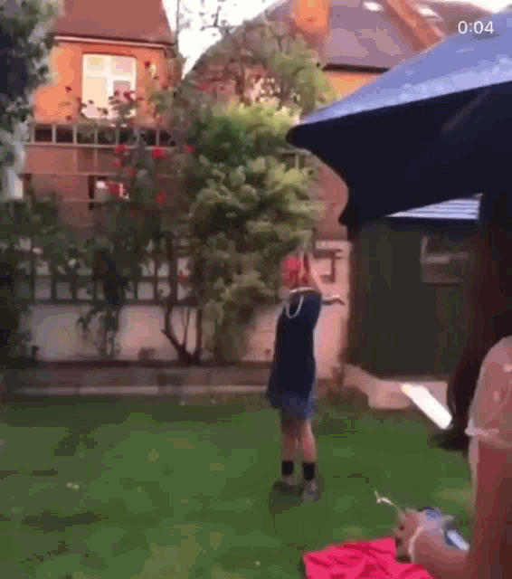 a woman is holding a cell phone in a backyard while a man throws a frisbee .
