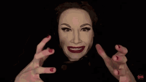 a woman with makeup on her face and red nails is making a funny face with her hands .