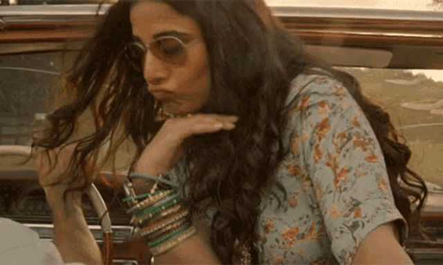 a woman with long hair and sunglasses is sitting in a car .