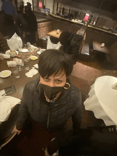 a woman wearing a mask sits in a restaurant