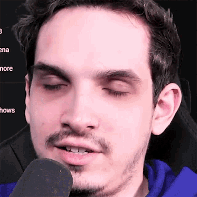 a man with a beard is talking into a microphone while wearing a blue hoodie .