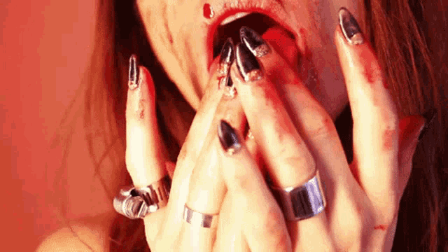 a woman with blood on her face and nails has rings on her fingers
