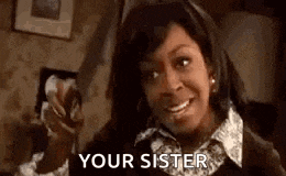 a woman is smiling and pointing at the camera with the words `` your sister '' written on her face .