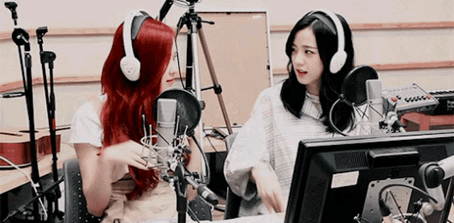 two women wearing headphones are sitting in front of microphones and a monitor .