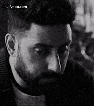 a man with a beard is looking down in a black and white photo .