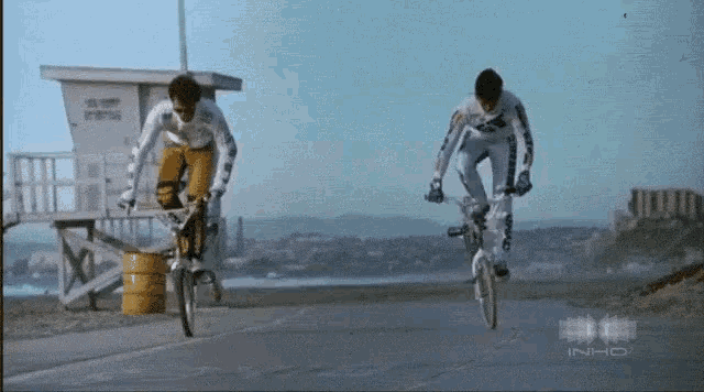 two men are riding bicycles in front of a lifeguard tower that says ' lifeguard ' on it