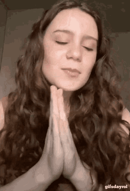 a woman with long curly hair is praying with her hands folded in prayer .