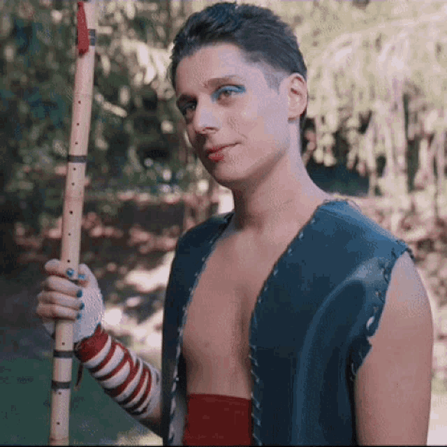 a man without a shirt is holding a wooden stick in his right hand