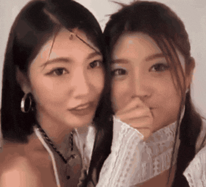 two women are standing next to each other and one is covering her mouth with her hand .
