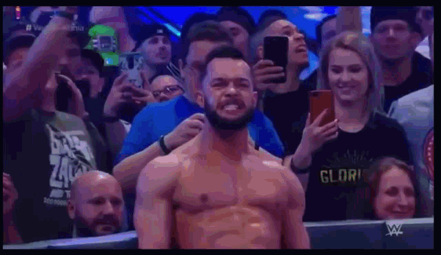 a man without a shirt is standing in front of a crowd while a woman takes a picture of him .