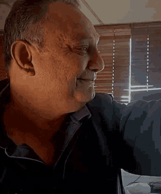a man is smiling in front of a window with blinds on it .