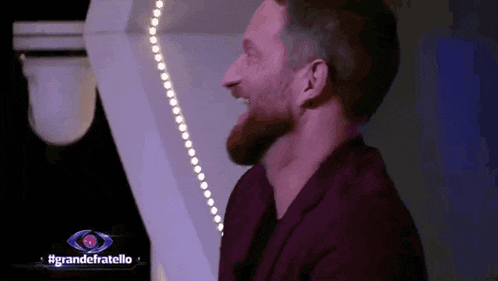 a man with a beard is laughing in front of a sign for grandefratello