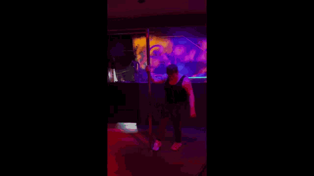 a man in a black tank top is standing on a pole in a dark room