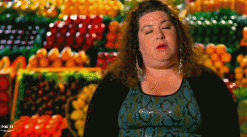 a woman is sitting in front of a display of fruits and vegetables with her eyes closed .