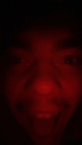 a close up of a person 's face in the dark with a red light behind it .