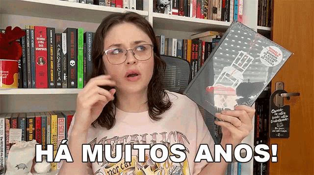 a woman holding a book in front of a bookshelf with the words ha muitos anos