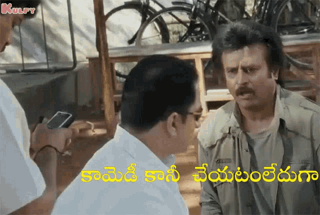 a man with a mustache is talking to another man while another man looks at his phone .