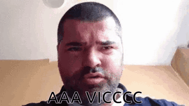 a man with a beard is making a funny face and the words aaa vicccc are on the bottom of his face .