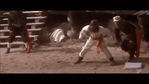 a group of men are standing in the dirt and one of them has a red sash around his waist