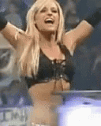 a blonde woman in a black bra and gloves is raising her arms in the air .