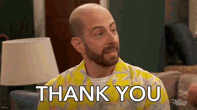a man in a yellow shirt says thank you in front of a lamp