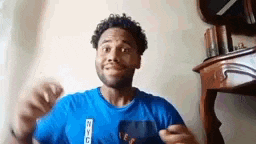 a man in a blue shirt is making a funny face while standing in front of a table .