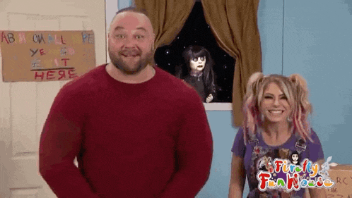 a man and a woman are standing next to each other in front of a window with a doll in the background .
