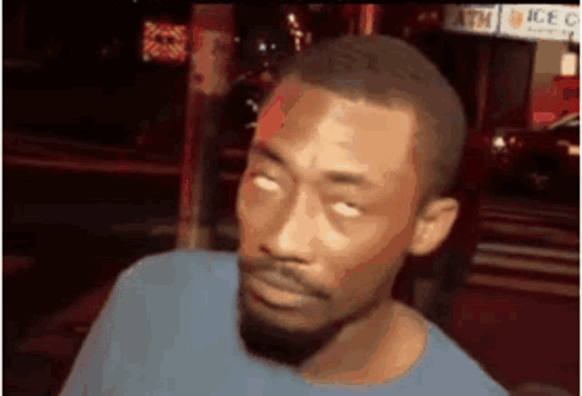 a man with a beard is making a funny face while standing in front of a sign that says atm .