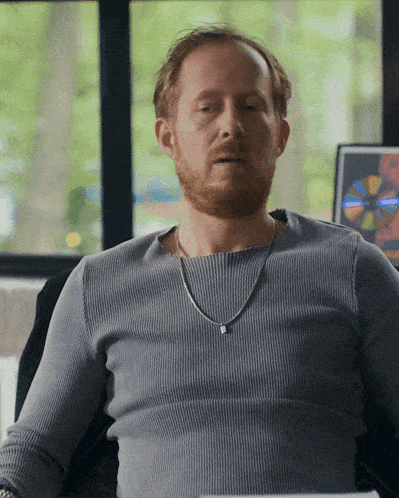 a man with a beard wearing a grey sweater and a chain around his neck