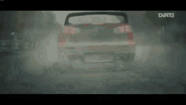 a red car is driving down a dirt road in the fog .