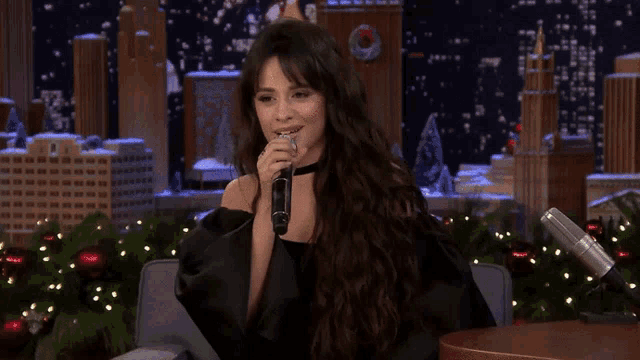 a woman with long hair is holding a microphone in front of a christmas tree .