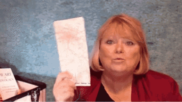 a woman in a red jacket holds a piece of paper in front of a sign that says hearts