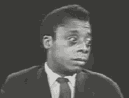 a black and white photo of a man in a suit and tie talking into a microphone .