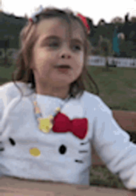 a little girl is sitting on a bench wearing a hello kitty shirt and a bow tie .
