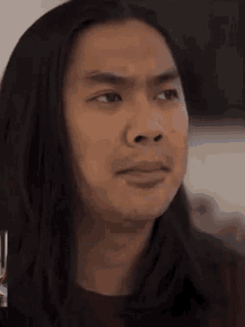 a man with long hair is making a funny face while looking at the camera .