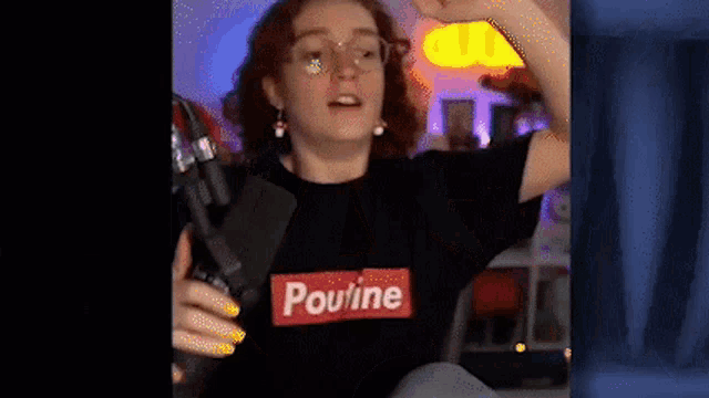 a woman wearing glasses and a pouline t-shirt is holding a microphone in her hand .