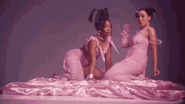 two women in pink dresses are kneeling on a bed