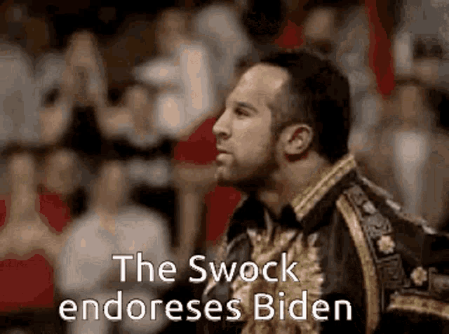 a man is standing in front of a crowd with the words `` the swock endorses biden '' written on the bottom .
