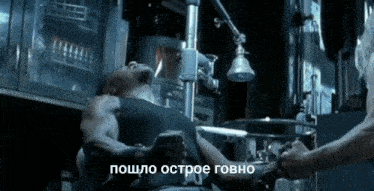a man in a black tank top is laying in an ambulance with russian writing on the bottom of the image