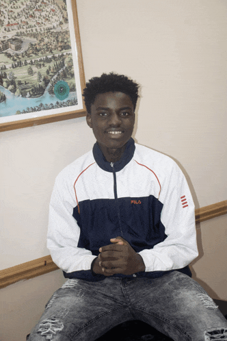 a man wearing a fila jacket sits in front of a picture