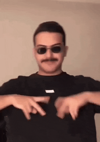 a man wearing sunglasses and a mustache is making a heart shape with his hands .