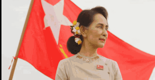 a woman with flowers in her hair stands in front of a large red flag