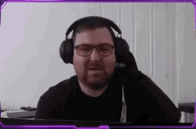 a man wearing glasses and headphones is sitting in front of a computer screen .