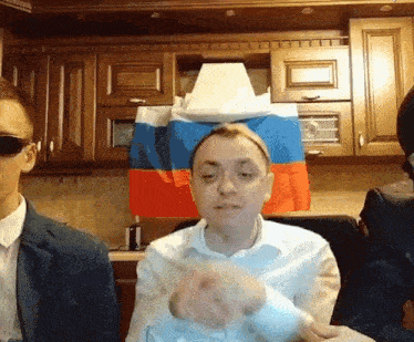 a man in a suit and tie is sitting in front of a russian flag .