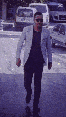 a man wearing sunglasses and a white jacket walking down a street