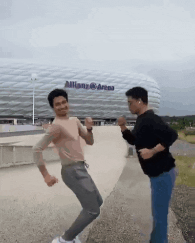 two men are dancing in front of a stadium that says allianz arena