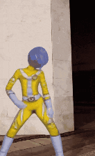 a yellow superhero with a blue helmet stands in front of a white wall