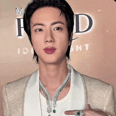 a man wearing a necklace and a ring stands in front of a sign that says id