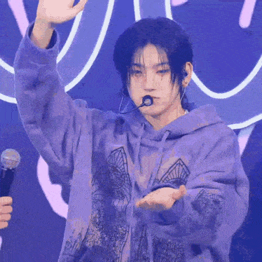 a young man is wearing a purple hoodie and holding a microphone .