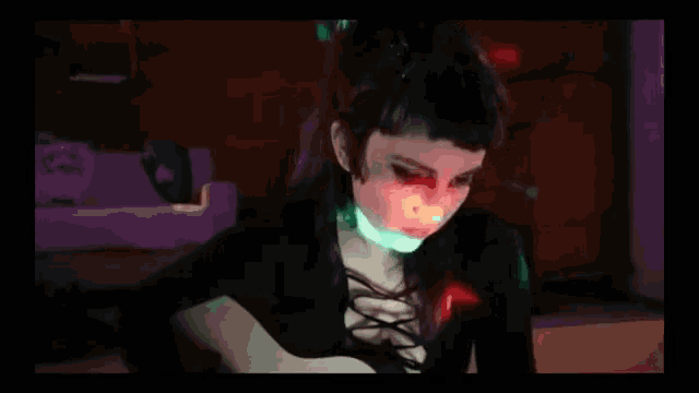 a woman is playing a guitar in a dark room with green and red lights .